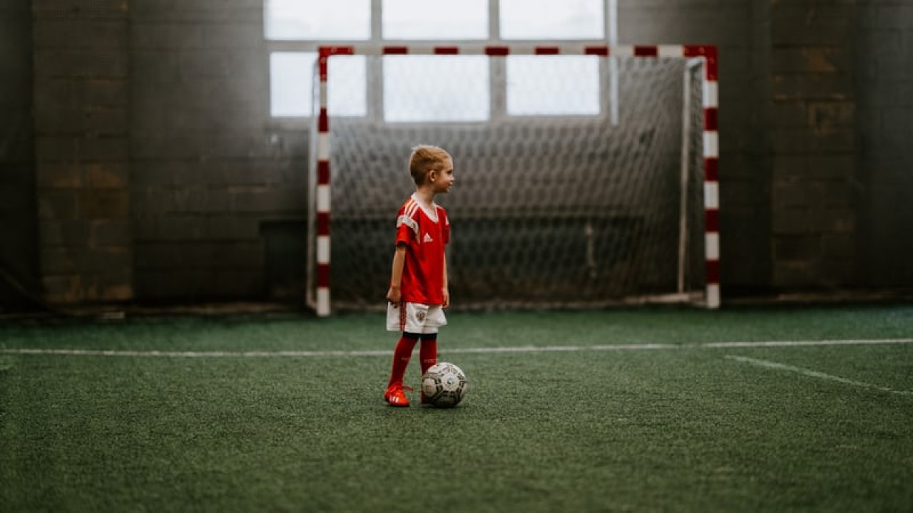 Liten gutt med fotball foran et mål